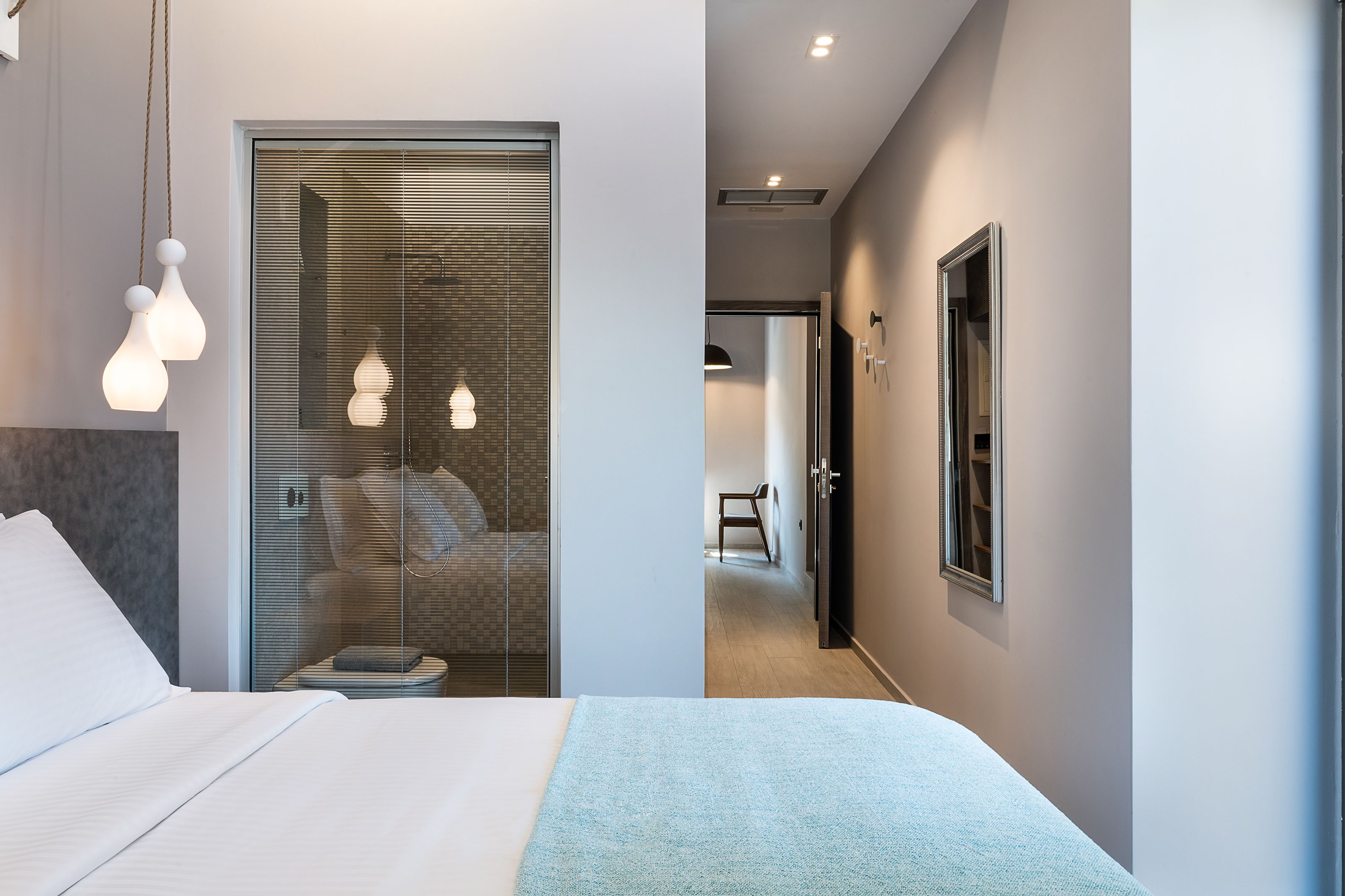 A modern hotel room with a bed, bedside table, and a walk-in closet with a mirror.