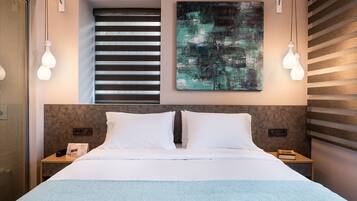 Une chambre d’hôtel moderne avec un grand lit, un tableau au mur et une fenêtre avec des stores.