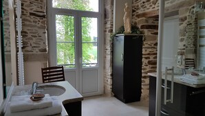 Un baño con pared de piedra, ventana con vista a follaje y un lavabo con toalla y mueble.