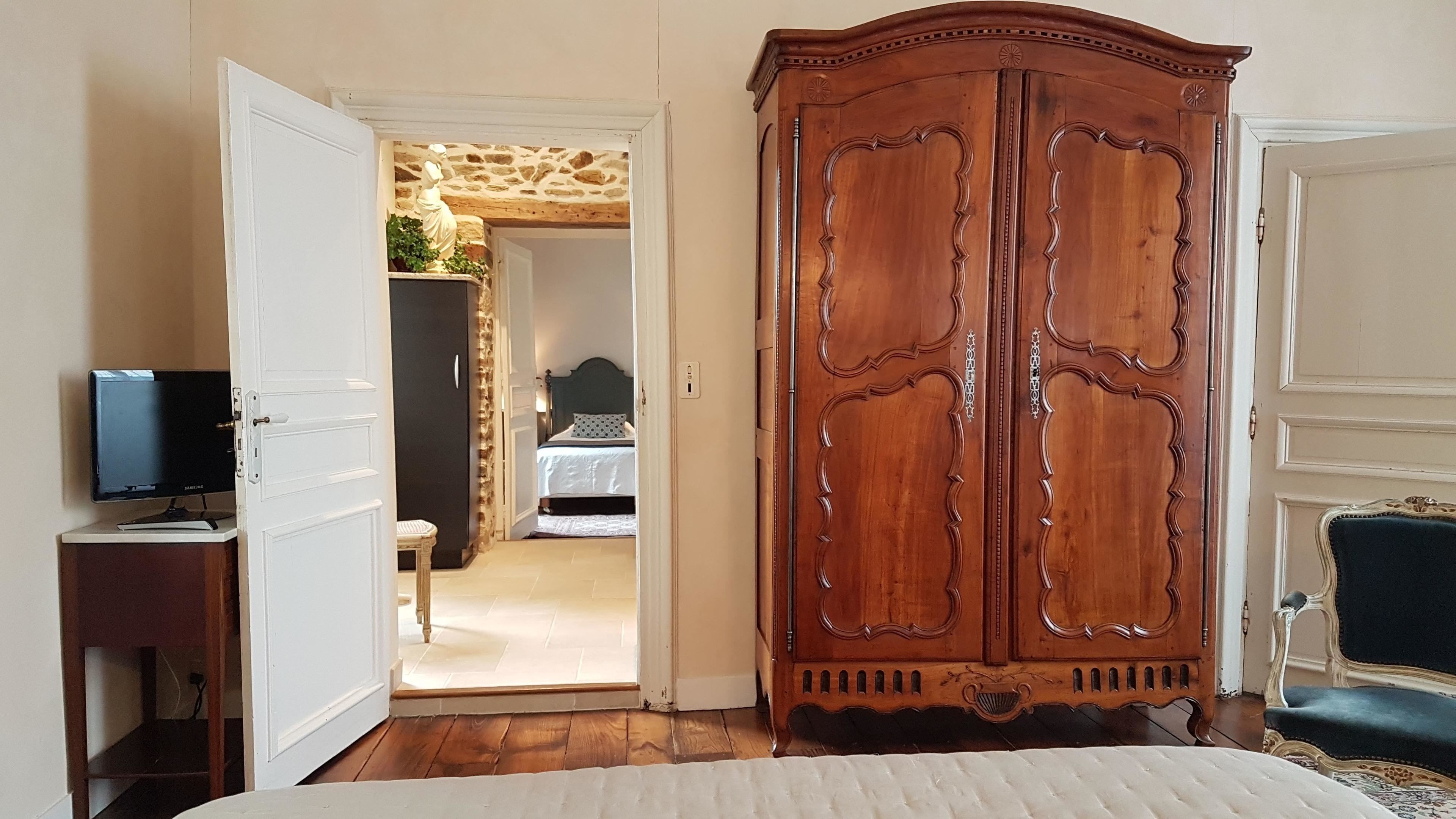 Un dormitorio con un armario de madera, una cama, un televisor sobre un pedestal y una pared de piedra al fondo.