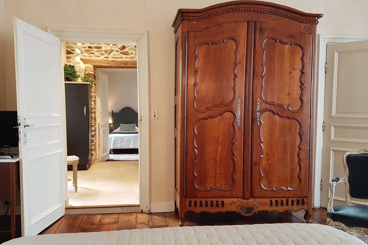 A bedroom with a wooden wardrobe, a bed, a television on a stand, and a stone wall in the background.
