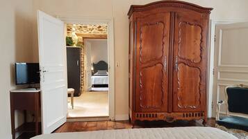 Un dormitorio con un armario de madera, una cama, un televisor sobre un pedestal y una pared de piedra al fondo.