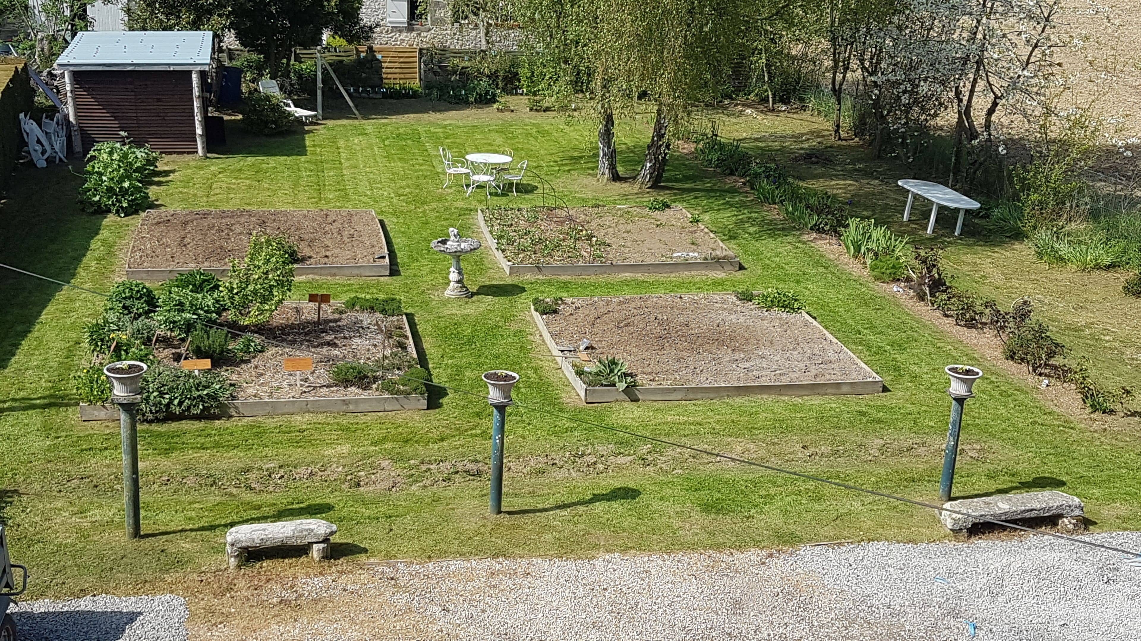Un jardín con parterres elevados, una zona de estar y un pequeño cobertizo.