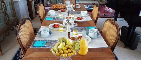 A dining table set with breakfast items, including croissants, strawberries, and a fruit bowl with grapes and oranges.