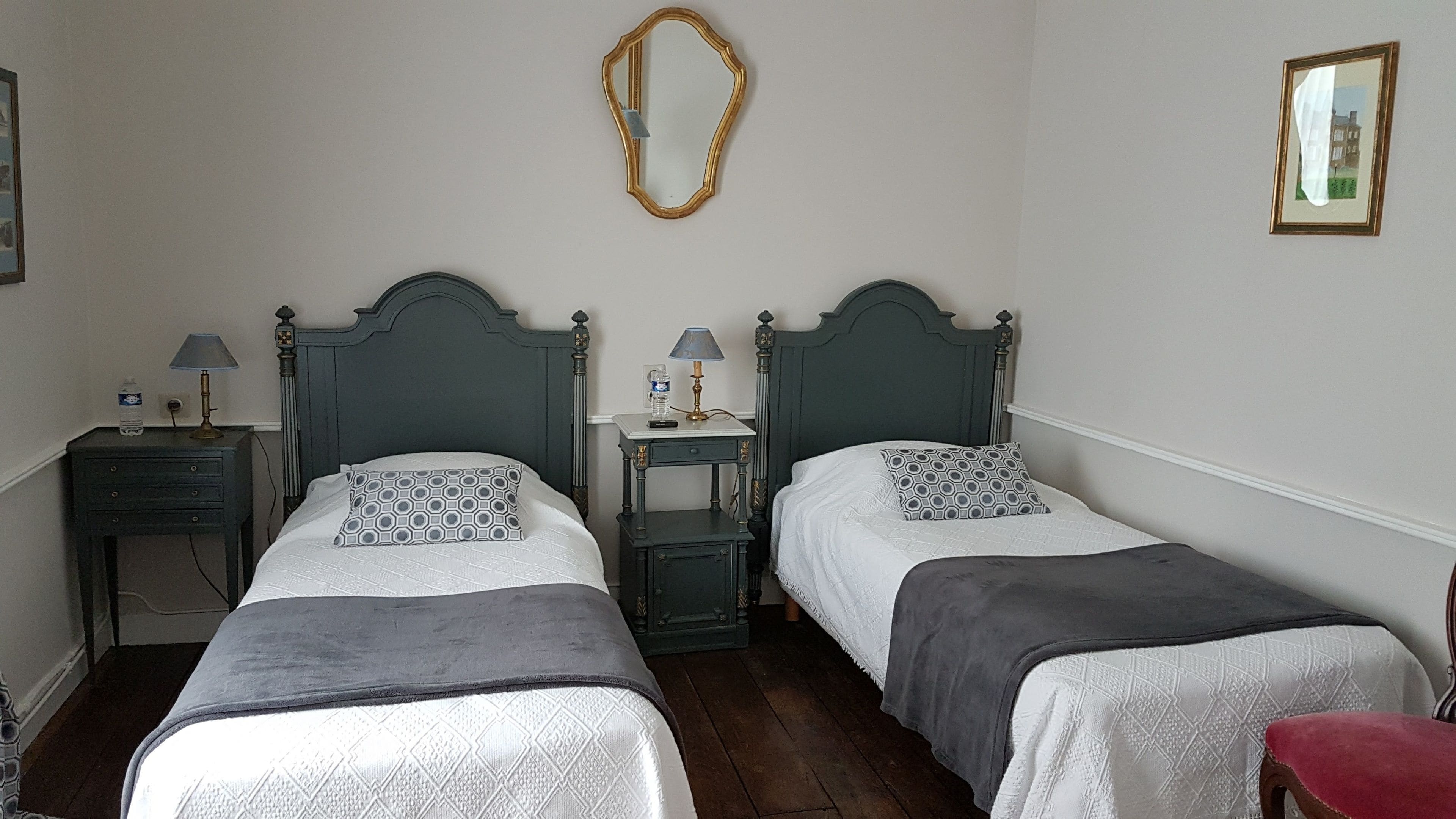 A room with two beds, each with a headboard, a bedside table, a lamp, and a mirror on the wall.
