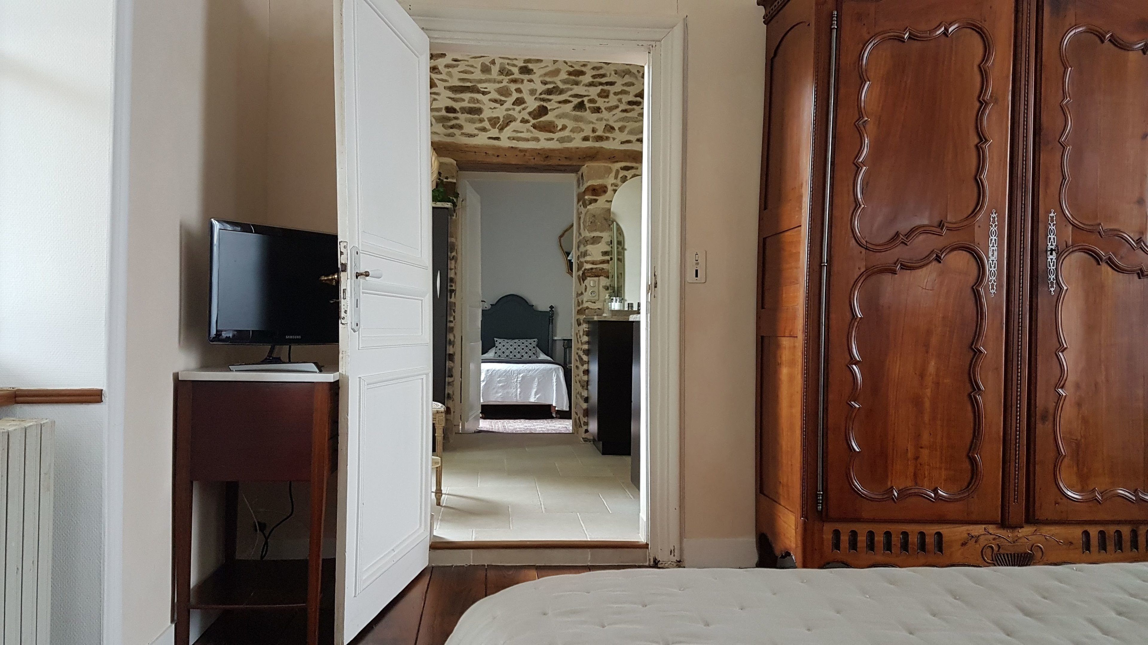 Une chambre à coucher avec un lit, un téléviseur posé sur un meuble, une armoire et un mur en pierre en arrière-plan.