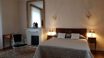 A bedroom with a large bed, two bedside lamps, a fireplace, a mirror, and a chair.