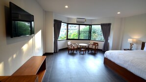 A hotel room with a large bed, a flat-screen TV mounted on the wall, a small round table with chairs, and a window with curtains. - Sila Pool Villa (Mae Rim)