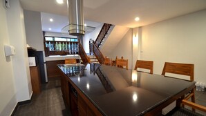 A spacious dining area with a large table, wooden chairs, a staircase, and a kitchen area in the background. - Sila Pool Villa (Mae Rim)