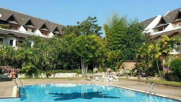 A swimming pool surrounded by a landscaped area with a row of buildings in the background. - Sila Pool Villa (Mae Rim)