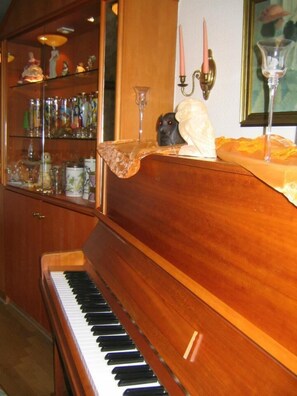 A grand piano with a glass display cabinet filled with decorative items behind it. - Hotel Gasthaus Kautz (Kamen)