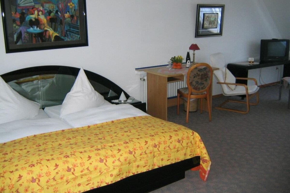 A hotel room with a bed, a desk, a chair, a television, and two framed pictures on the wall.