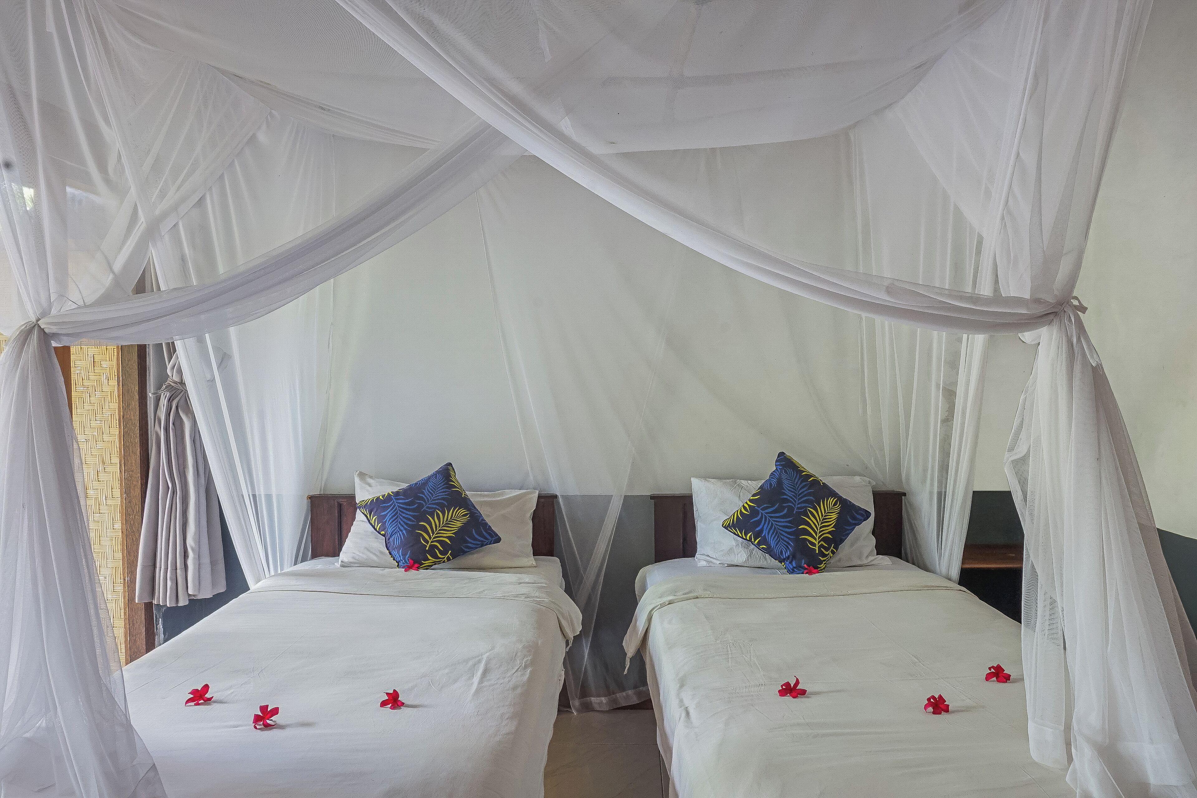 A room with two beds, each with white bedding and blue decorative pillows.