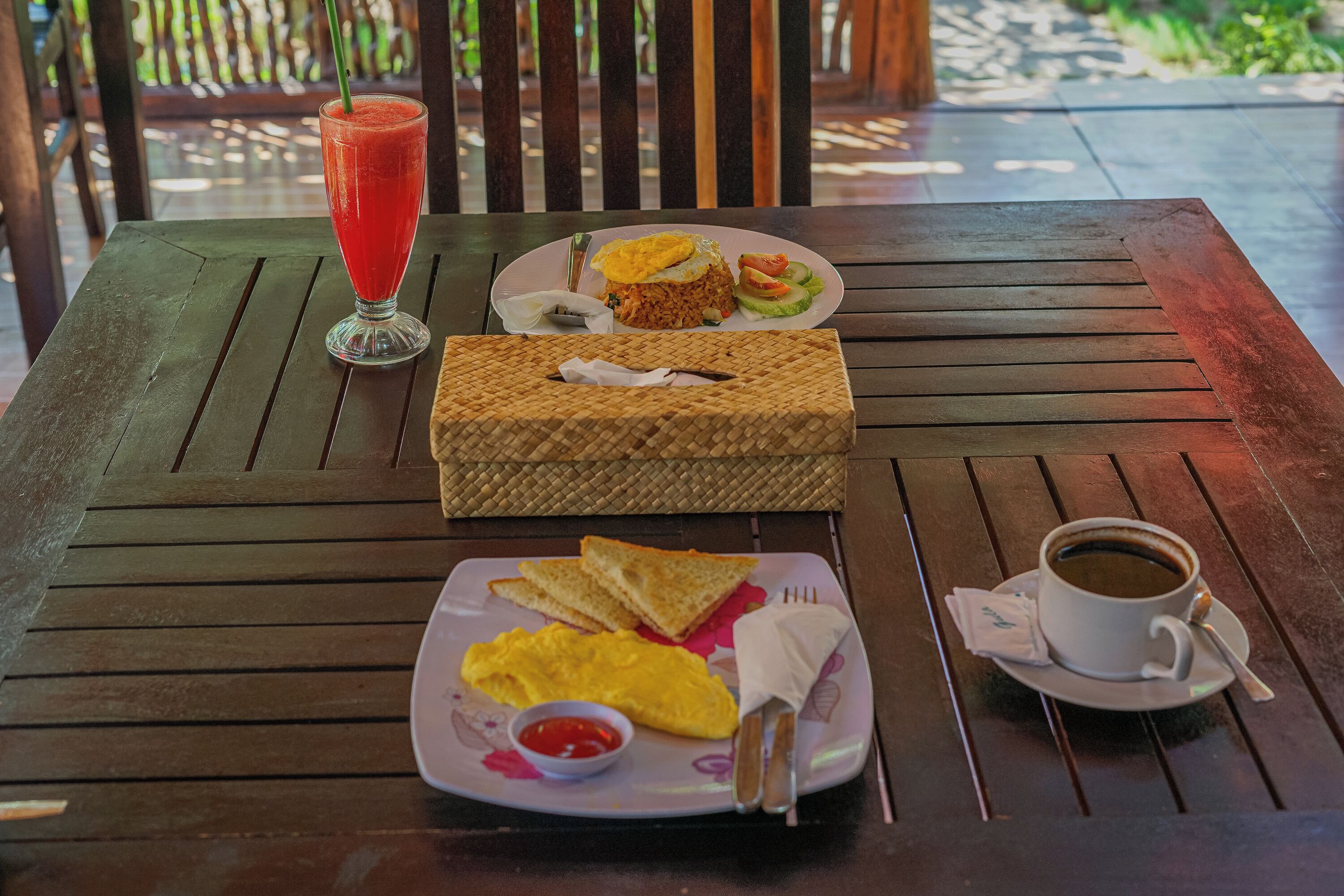 Una mesa de madera con alimentos para el desayuno, incluyendo tostadas, huevos revueltos, un batido y una taza de café.