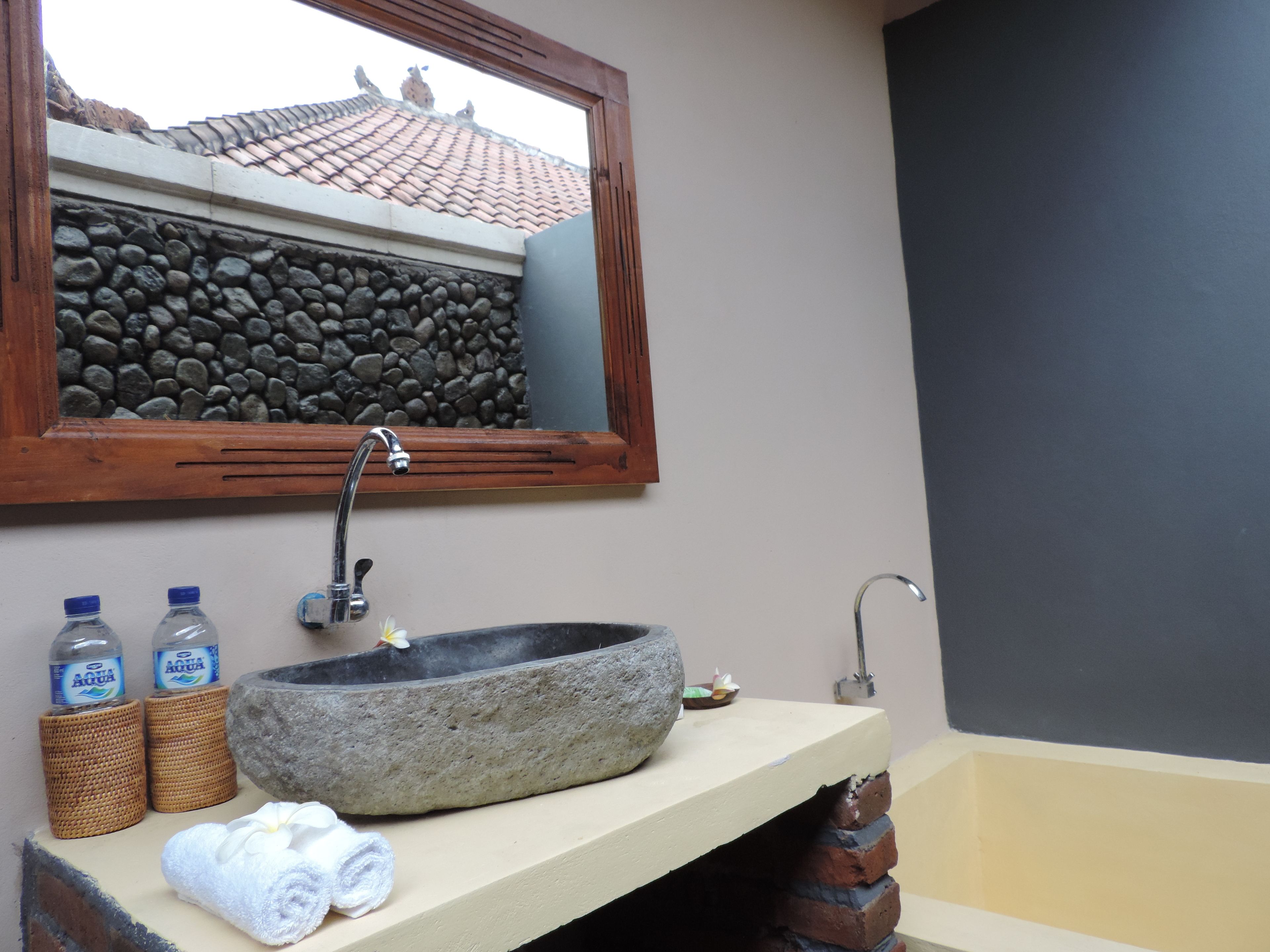 Casa de banho com lavatório de pedra, duas garrafas de água, uma toalha e um espelho.