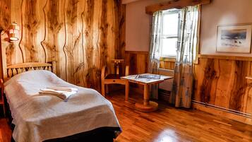 Relax in a warm, inviting room with a neatly made bed, wooden table, and a window offering a view of the outdoors.