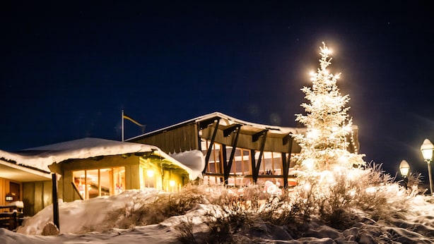 Un bâtiment dont le toit est recouvert de neige, avec un sapin de Noël illuminé devant.