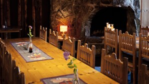 Une longue table à manger en bois, avec des chaises, un vase rempli de fleurs et un chandelier.