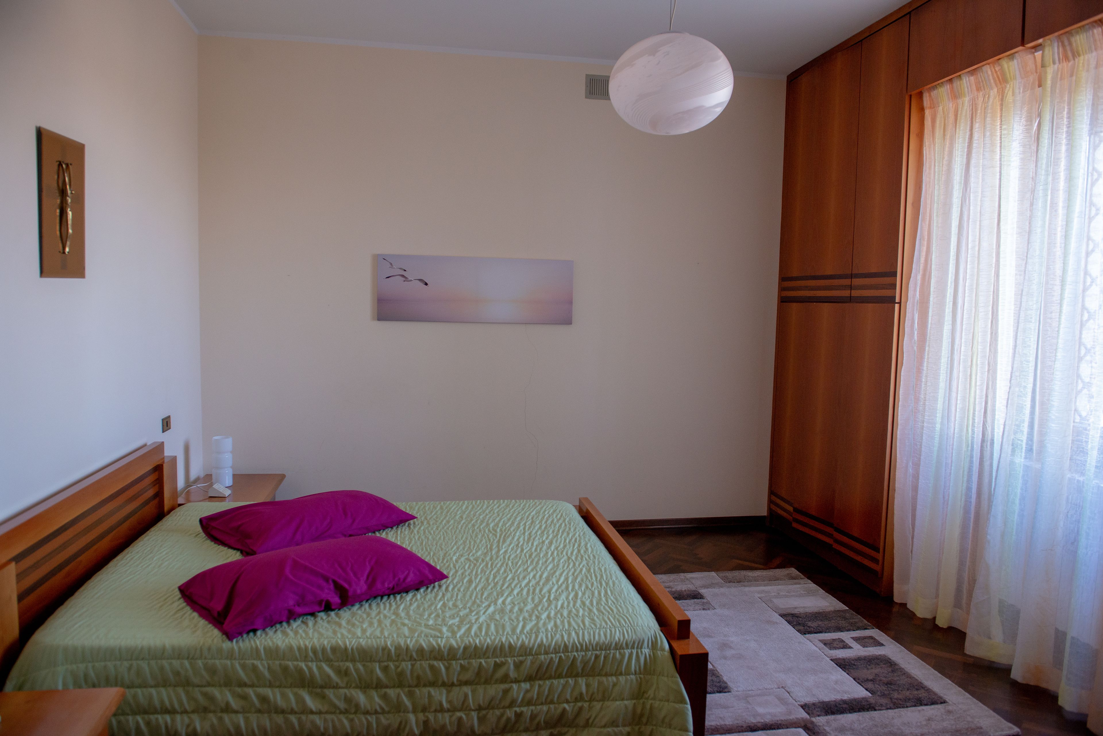 Une chambre à coucher avec un lit, des oreillers, un tableau, une table de chevet et une armoire.