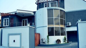 Un edificio moderno con fachada de vidrio curvo, una terraza de madera y un equipo de aire acondicionado.