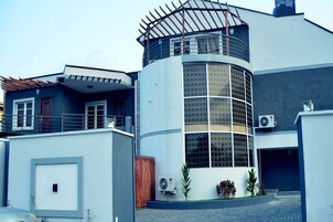 Un edificio moderno con fachada de vidrio curvo, una terraza de madera y un equipo de aire acondicionado.