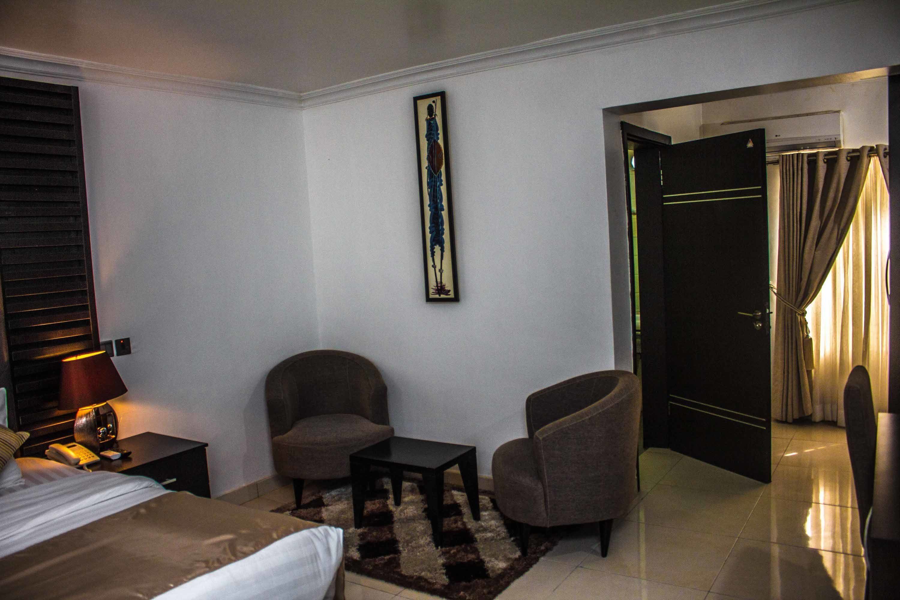 Une chambre d’hôtel avec un lit, deux fauteuils, une petite table, une lampe et un tableau au mur.