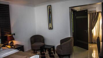 Une chambre d’hôtel avec un lit, deux fauteuils, une petite table, une lampe et un tableau au mur.