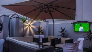 Un patio con mobiliario exterior, una sombrilla grande y un televisor montado en la pared.