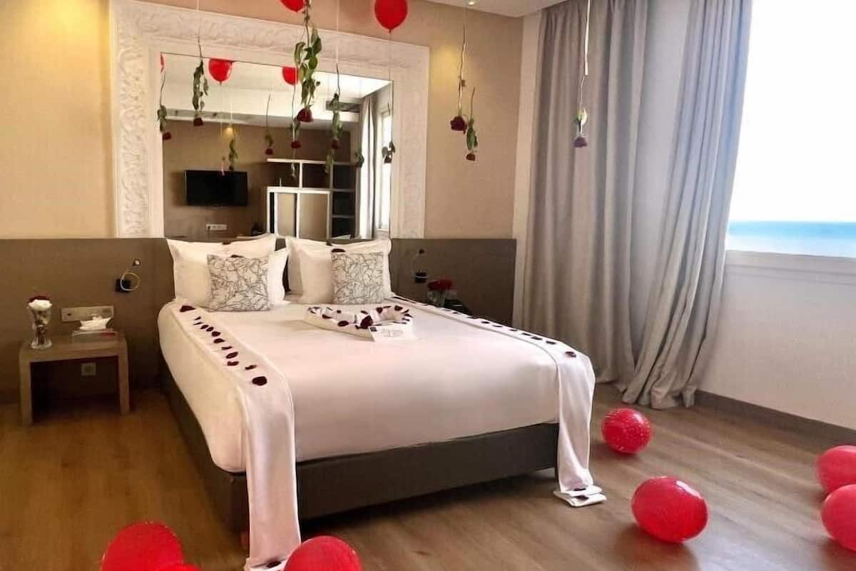 A hotel room with a large bed, a TV, and a view of the sea.