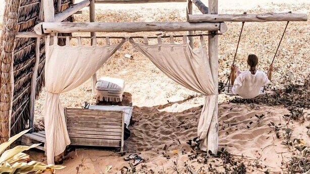 Una cabaña playera con techo de paja, un banco y un columpio.