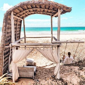 A beach hut with a thatched roof, a bench, and a swing. - Pura Vida Tofo Beach House (Tofo)