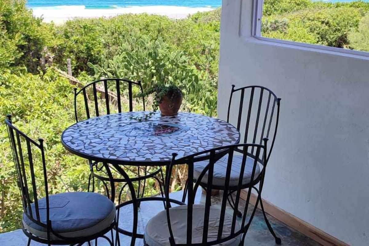 A round table with four chairs, a potted plant, and a view of the ocean.