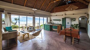 Amplia sala de estar con un ventanal grande con vista a la playa, una zona de cocina y una mesa de comedor.