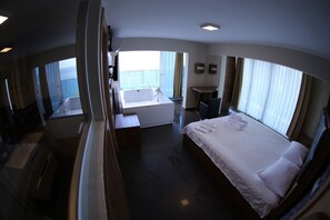 A hotel room with a large bed, a separate bathroom with a bathtub, a small desk, and a view of the sea. - Bayraktar Hotel (Akcakoca)