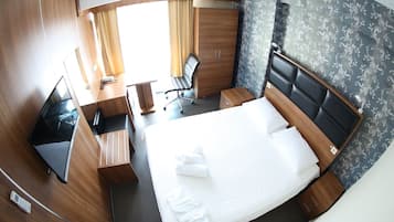 Habitación de hotel pequeña con cama, escritorio, silla y televisor.