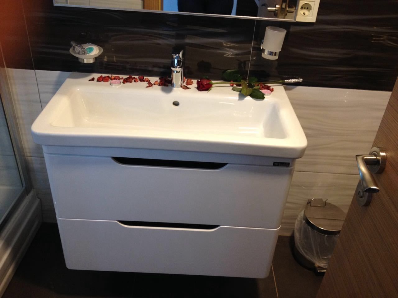 A bathroom with a white sink, a mirror, and a trash can.