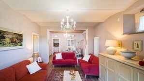 A spacious living room with red sofas, a chandelier, and a dining area in the background. - Casale di Vera (Cortona)