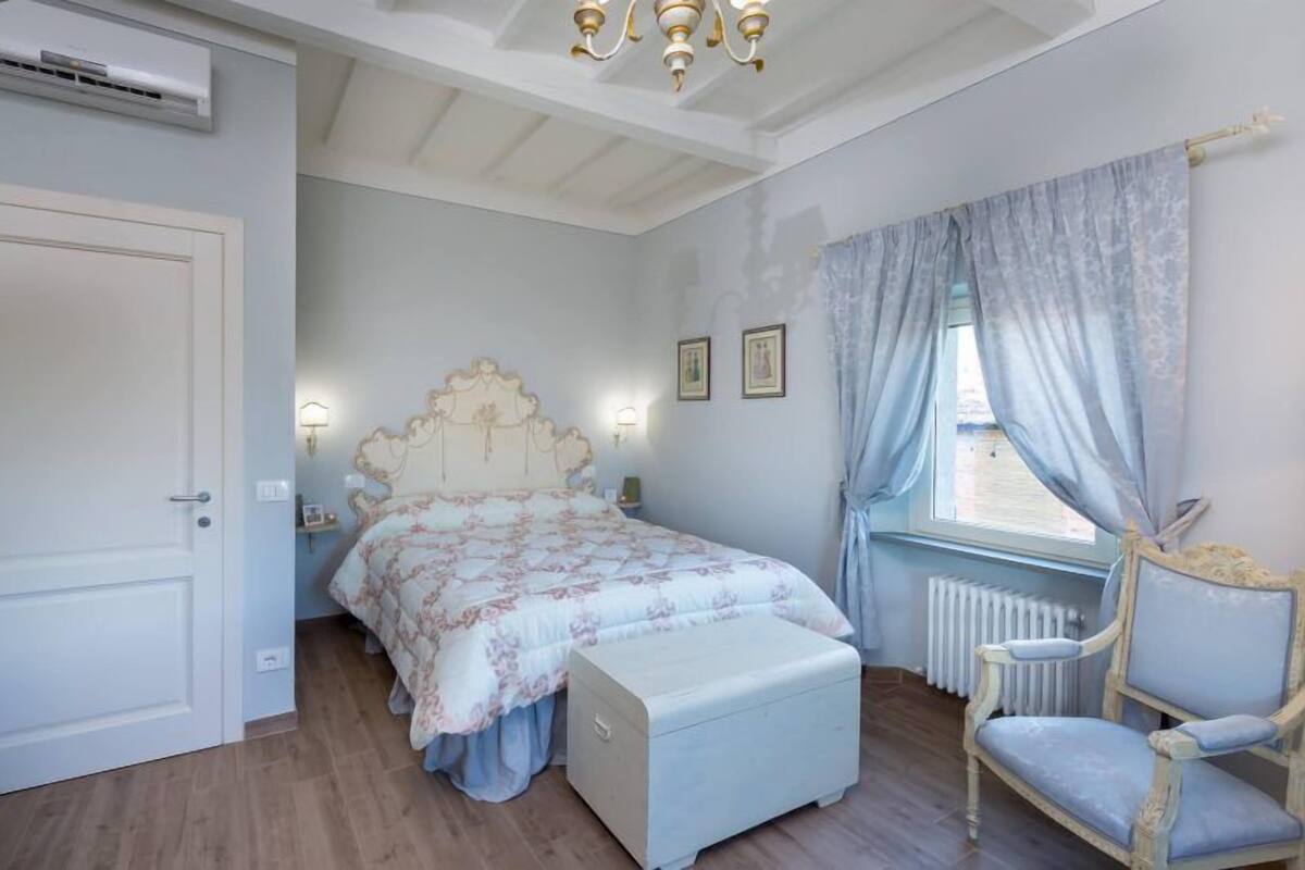 A bedroom with a bed, a chair, a radiator, and a window with curtains.