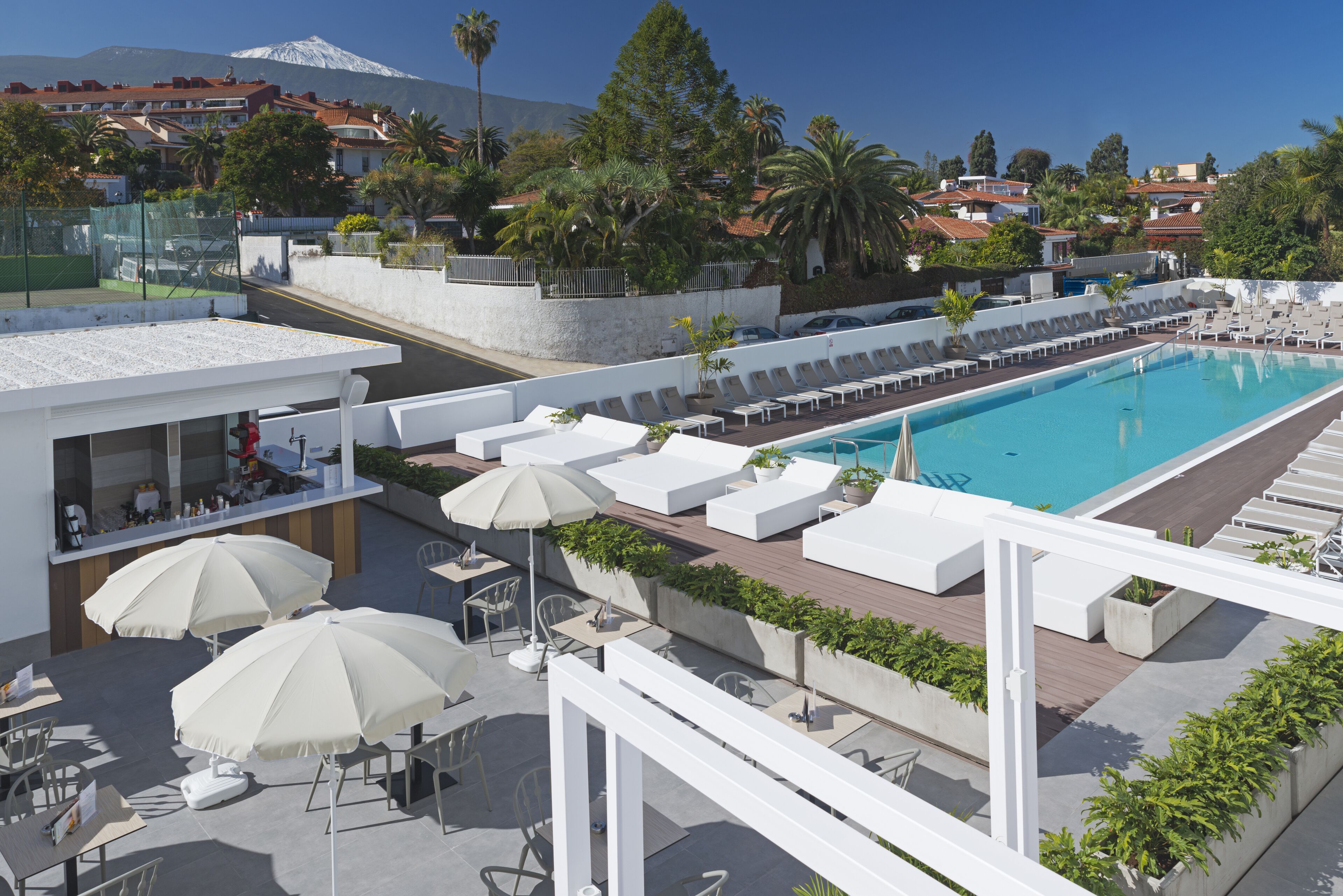 A rooftop pool area with lounge chairs and umbrellas, a bar, and a view of a mountain.