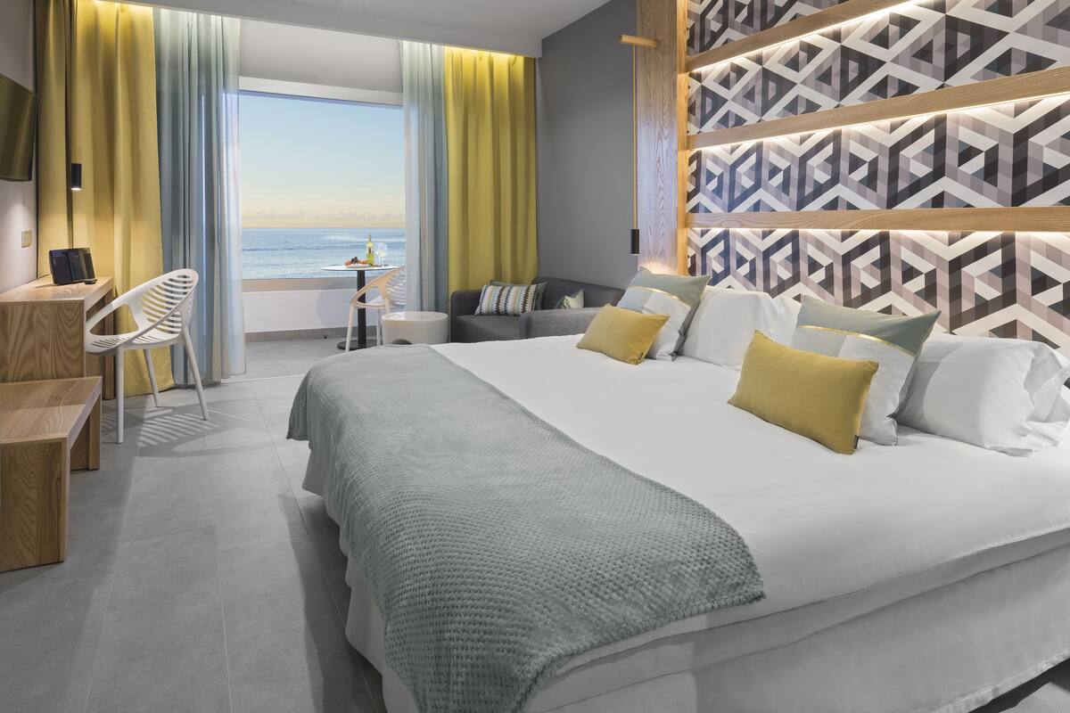 A modern hotel room with a large bed, a desk, and a view of the ocean.