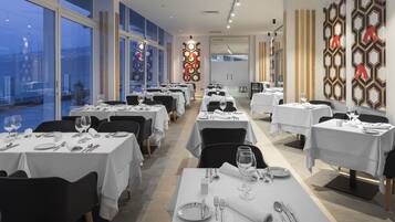 A restaurant with multiple tables set for dining, large windows, and decorative wall panels.