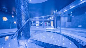 Un área de piscina interior moderna con suelo de baldosas, una columna central y una barandilla de metal.