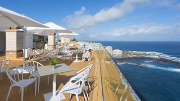 A deck with white chairs and tables, overlooking the ocean.