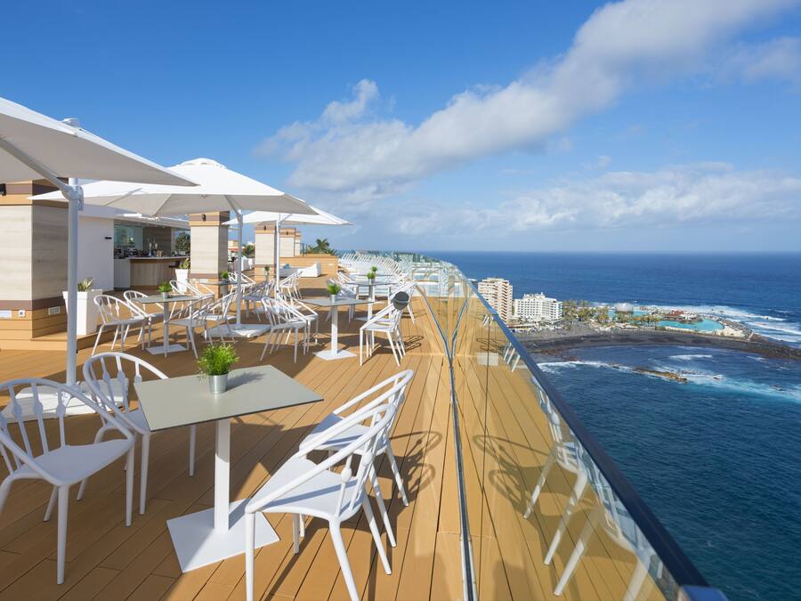 A deck with white chairs and tables, overlooking the ocean.