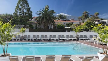 A pool with lounge chairs, surrounded by potted plants and a mountain in the background.