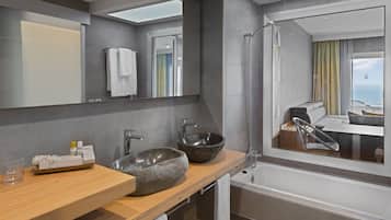 A modern bathroom with a large mirror, a stone sink, a bathtub, and a view of a balcony with a sofa.