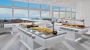 Montaje de bufé con diversos alimentos y vistas al mar a través de amplias ventanas.