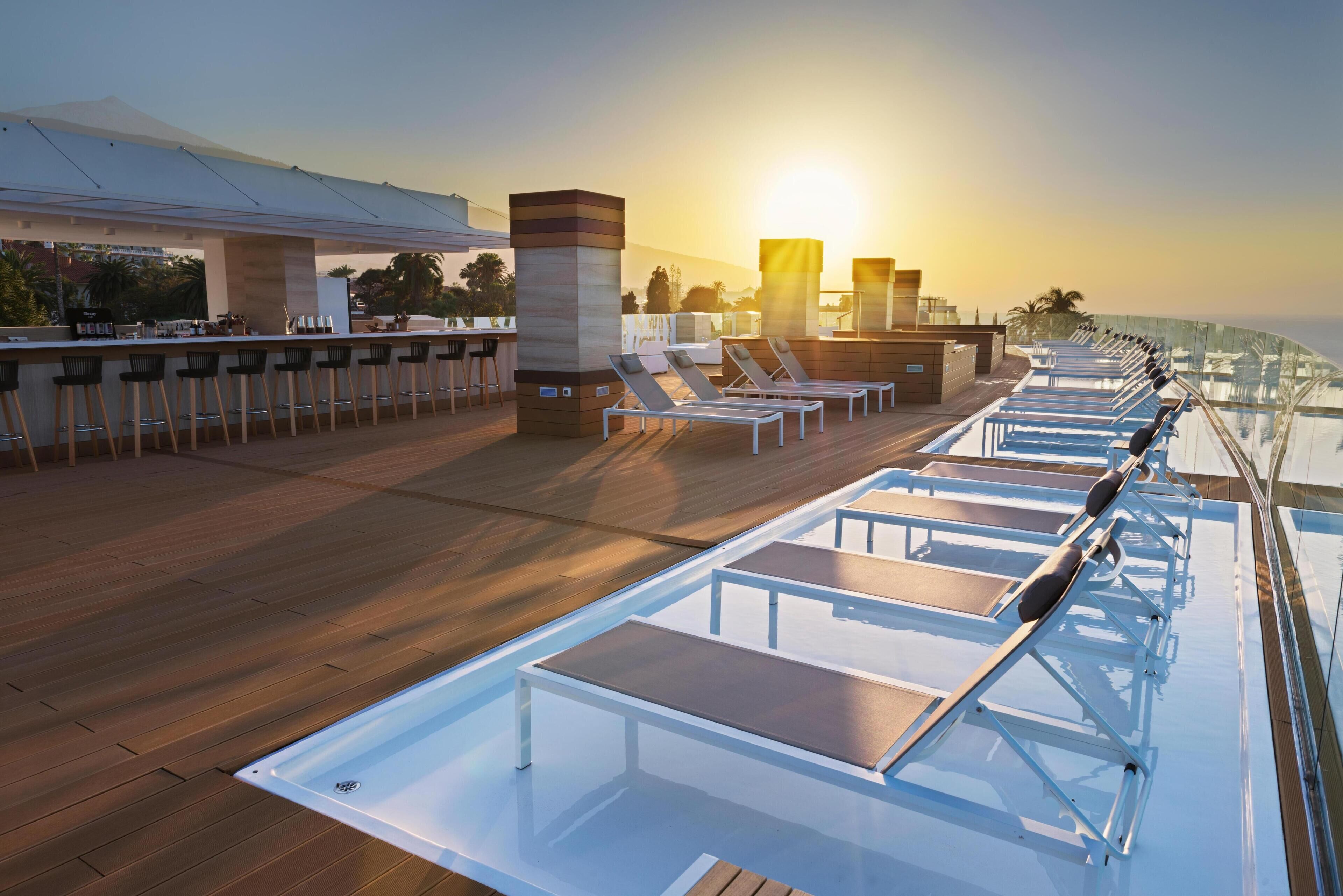 A sunlit deck with lounge chairs and a bar area, overlooking a body of water.