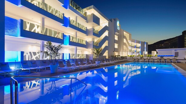 Un hotel moderno con piscina, varios balcones y una fachada bien iluminada.