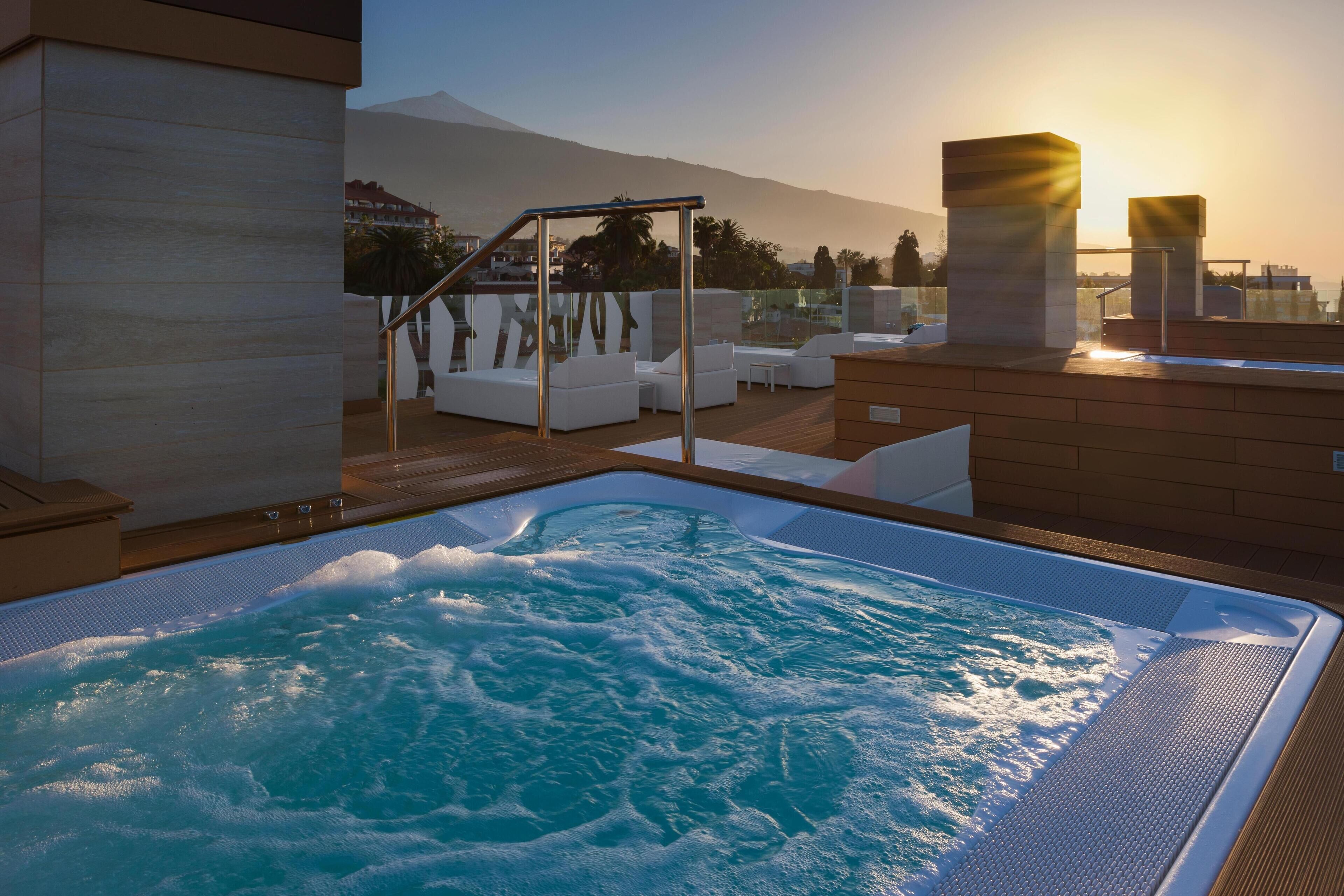 Un jacuzzi con vistas a montañas y al atardecer.